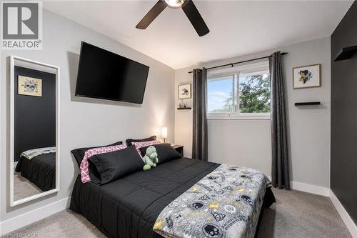 Carpeted room featuring a ceiling fan, a wall-mounted television, and a window with a dark curtain rod. Digitally enhanced. - 35 Vicmount Drive, Kitchener, ON 