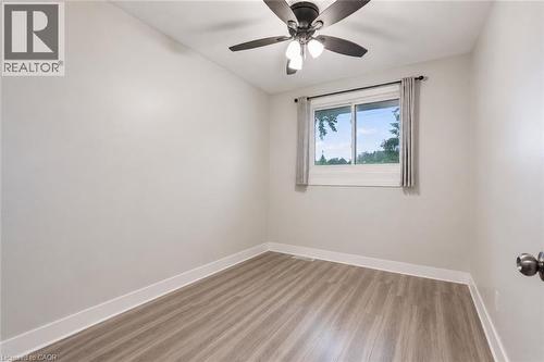 Neutral wall paint with white trim, wood-finish  flooring, a window with a white frame, and a ceiling fan with integrated lighting. Digitally enhanced - 35 Vicmount Drive, Kitchener, ON 
