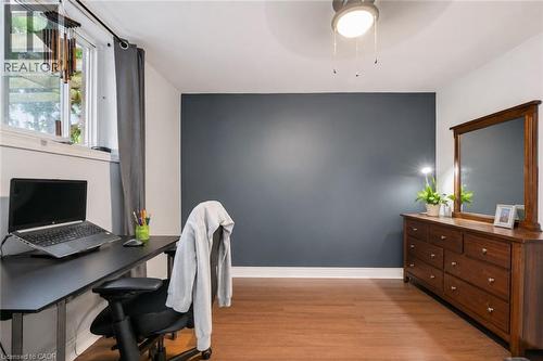 Room featuring a dark accent wall, wood-finish flooring, a window with grey drapes, and a ceiling-mounted light fixture. Digitally enhanced. - 35 Vicmount Drive, Kitchener, ON 