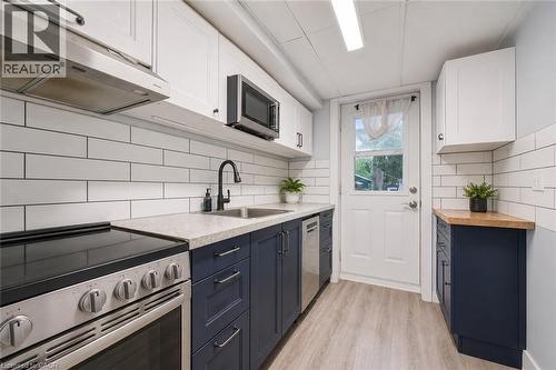 Modern kitchen featuring stainless steel appliances, two-tone cabinetry with black hardware, white subway tile backsplash, light-toned countertops, and wood-finish flooring. Digitally enhanced. - 35 Vicmount Drive, Kitchener, ON 