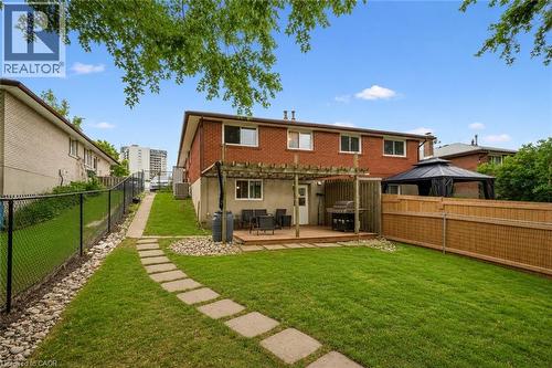 Expansive backyard featuring a manicured lawn, a stone paver pathway, a wooden deck with a pergola, a privacy fence, and a brick exterior. Digitally enhanced. - 35 Vicmount Drive, Kitchener, ON 