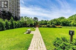 Expansive green space featuring a paver stone pathway, mature trees, manicured hedges, and a black metal fence - 