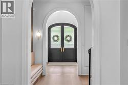 Arched entryway featuring double doors with glass panels, light wood-finish flooring, and a built-in wall sconce - 