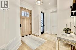 Entryway featuring a natural wood door with glass panes, wood-finish flooring, white paneled walls, and crown molding - 