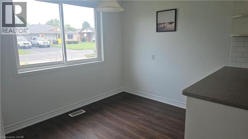 Bright interior space featuring a large window, dark wood-finish flooring, white baseboards, and a white subway tile backsplash - 58 Belwood Crescent, Kitchener, ON 