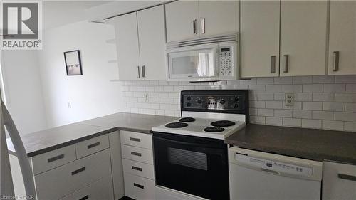 Kitchen featuring white cabinetry with brushed nickel hardware, solid surface countertops, white subway tile backsplash, built-in microwave, and an electric range - 58 Belwood Crescent, Kitchener, ON 