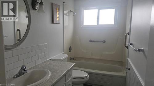 Bathroom featuring a vanity with an integrated sink, a light-colored countertop, white subway tile backsplash, a circular mirror, and a bathtub with shower - 58 Belwood Crescent, Kitchener, ON 