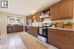 Kitchen featuring wood cabinetry, stainless steel appliances, granite countertops, a tiled backsplash, and recessed lighting - 