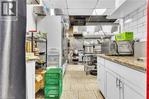 Commercial kitchen featuring tiled flooring, white subway tile backsplash, white cabinetry with silver-tone hardware, and an integrated stainless steel range hood - 155 Highland Road E, Kitchener, ON 