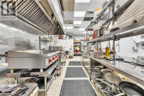 Commercial-grade kitchen featuring stainless steel appliances, a large griddle, extensive stainless steel shelving, and durable non-slip floor mats - 155 Highland Road E, Kitchener, ON 