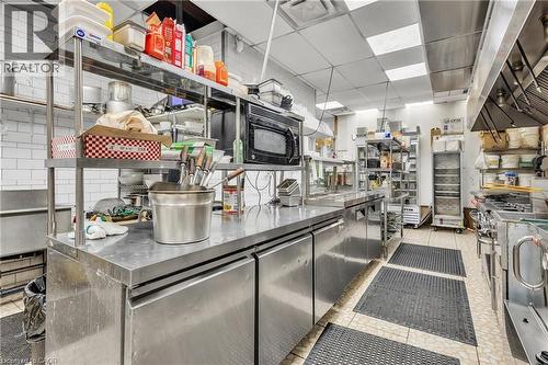Professional-grade kitchen featuring extensive stainless steel countertops and appliances, subway tile backsplash, and recessed ceiling lighting - 155 Highland Road E, Kitchener, ON 