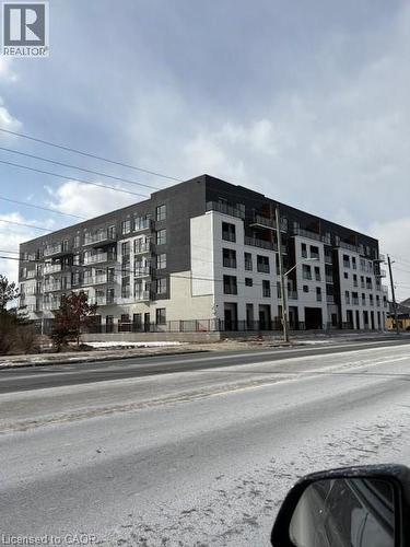 Contemporary multi-story building featuring a facade of black and white panels, multiple balconies with glass railings, and ground-level fencing - 1936 Rymal Road E Unit# 516, Hannon, ON - Outdoor With Facade