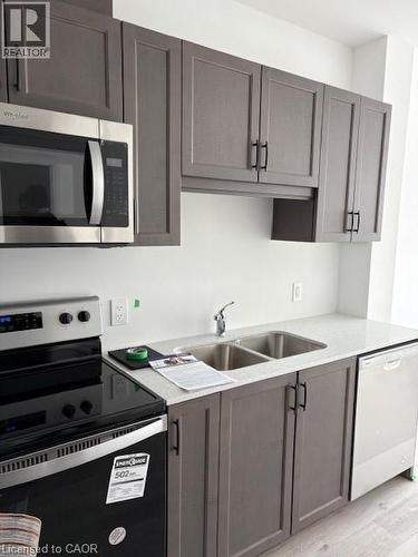 Modern kitchen featuring gray shaker-style cabinetry with matte black hardware, stainless steel appliances, a double basin sink, and wood-finish flooring - 1936 Rymal Road E Unit# 516, Hannon, ON - Indoor Photo Showing Kitchen With Double Sink