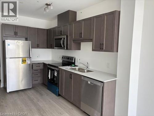L-shaped kitchen featuring wood-finish cabinetry, stainless steel appliances, and white countertops - 1936 Rymal Road E Unit# 516, Hannon, ON - Indoor Photo Showing Kitchen With Double Sink
