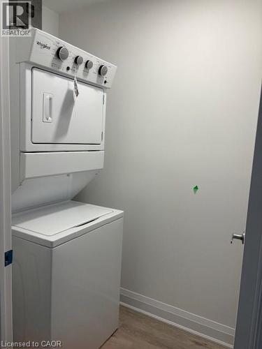 Dedicated laundry area featuring a stacked washer and dryer unit, light wood-finish flooring, and white baseboards - 1936 Rymal Road E Unit# 516, Hannon, ON - Indoor Photo Showing Laundry Room