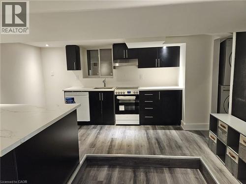 Modern kitchen featuring dark cabinetry, light countertops, wood-finish flooring, a full suite of appliances including a dishwasher and range, and recessed lighting - 134 E Bridgeport Road E Unit# Lower, Waterloo, ON 