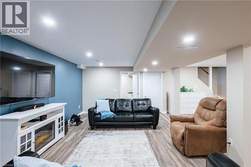 Finished lower level featuring wood-finish flooring, recessed lighting, a built-in media console with an electric fireplace, and a light blue accent wall - 28 Mcgibbon Court, Kitchener, ON 