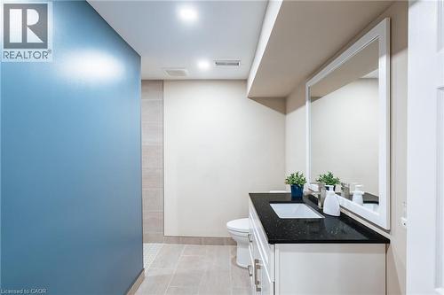 Bathroom vanity featuring a dark countertop with an integrated sink, white cabinetry with silver-toned hardware, and a large framed mirror - 28 Mcgibbon Court, Kitchener, ON 