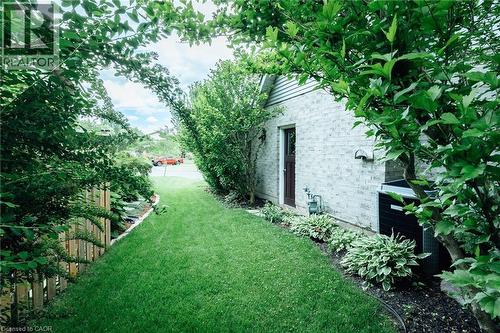 Side yard featuring a lush lawn, mature perimeter landscaping, and a privacy fence - 28 Mcgibbon Court, Kitchener, ON 