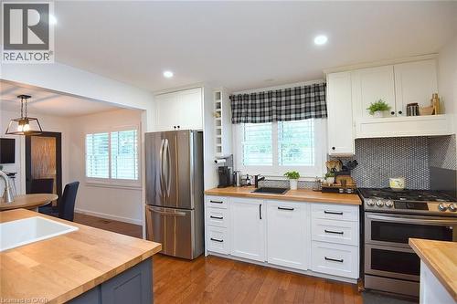 Kitchen featuring white cabinetry, butcher block countertops, stainless steel appliances, a black penny tile backsplash, and wood-finish flooring - 8 Sheridan Boulevard, Simcoe, ON 