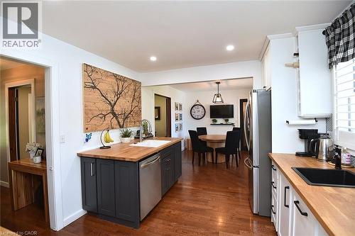Contemporary kitchen featuring wood-finish flooring, butcher block countertops, recessed lighting, white cabinetry, and a dark island with a built-in dishwasher - 8 Sheridan Boulevard, Simcoe, ON 