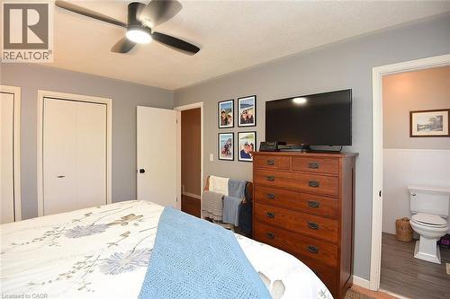 Bedroom featuring a ceiling fan with integrated lighting, bi-fold closet doors, and an open doorway leading to a bathroom with a white toilet and wainscoting - 8 Sheridan Boulevard, Simcoe, ON 