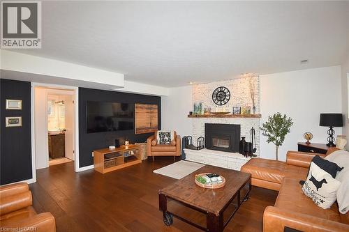 Living area featuring wood-finish flooring, a white-painted brick fireplace with a wood mantel, and a black accent wall - 8 Sheridan Boulevard, Simcoe, ON 
