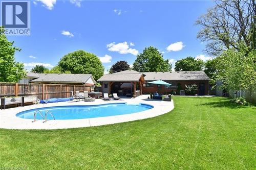 Expansive backyard featuring an in-ground swimming pool with surrounding concrete decking, a covered patio area, and a large manicured lawn - 8 Sheridan Boulevard, Simcoe, ON 