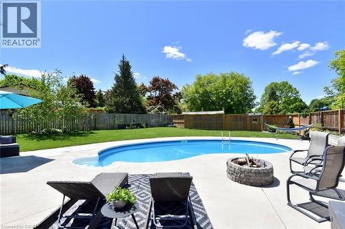 Resort-style backyard featuring an in-ground swimming pool, concrete patio, and a built-in stone fire pit - 8 Sheridan Boulevard, Simcoe, ON 
