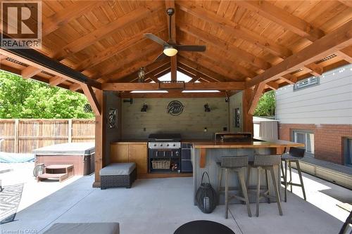 Outdoor living area featuring a vaulted wood-finish ceiling with exposed beams, a built-in outdoor kitchen with grill, a bar with seating for three, a ceiling fan, and concrete patio flooring - 8 Sheridan Boulevard, Simcoe, ON 