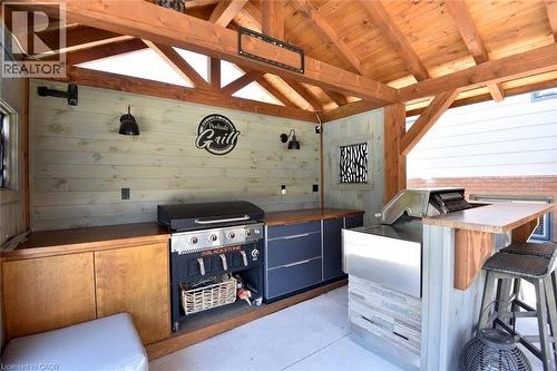 Covered outdoor kitchen featuring a wood-beam ceiling, plank wood walls, built-in cabinetry, and integrated cooking appliances - 8 Sheridan Boulevard, Simcoe, ON 