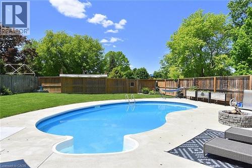Private backyard featuring a curved inground pool, concrete patio, stone fire pit, and wood perimeter fencing - 8 Sheridan Boulevard, Simcoe, ON 