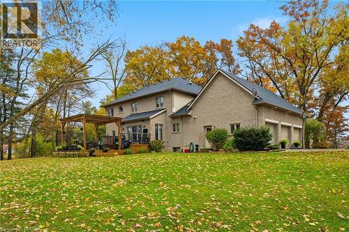 Spacious rear exterior featuring a multi-level deck with a wooden pergola, brick facade, and an attached three-car garage - 271 Windham Rd 14, Simcoe, ON 