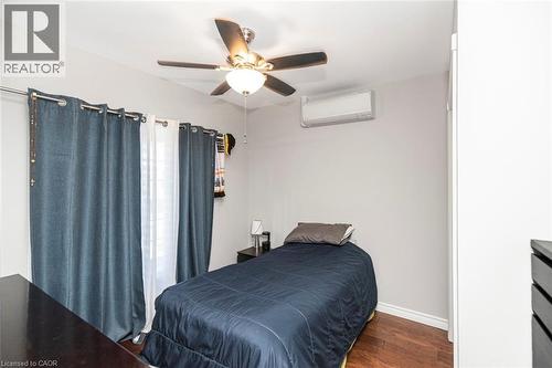 Bedroom featuring wood-finish flooring, a ceiling fan with integrated lighting, and a wall-mounted climate control unit - 38 Fairleigh Avenue N, Hamilton, ON 