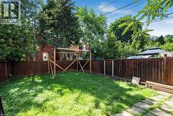 Expansive backyard featuring a lush lawn, privacy fencing, mature trees, and a red brick exterior - 