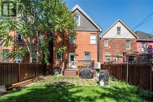 Rear exterior featuring a wood deck, red brick facade, wood fencing, and a grassy yard - 38 Fairleigh Avenue N, Hamilton, ON 