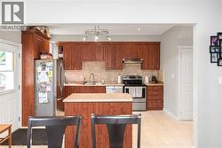 Kitchen featuring rich wood cabinetry, stainless steel appliances, a center island with a light-toned countertop, a neutral tile backsplash, and light-toned tile flooring - 