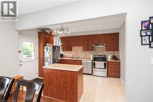 Kitchen featuring wood-finish cabinetry, stainless steel appliances, a center island with a light-toned countertop, and tiled flooring - 38 Fairleigh Avenue N, Hamilton, ON 