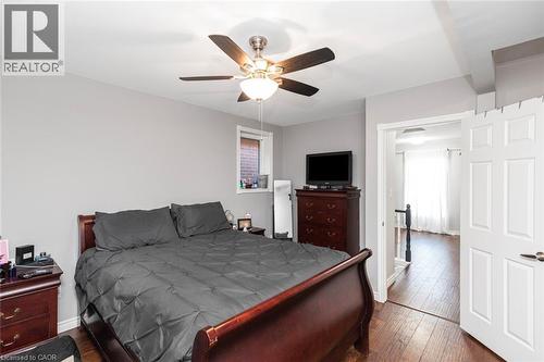 Bedroom featuring wood-finish flooring, a ceiling fan with integrated lighting, and a window with brick exterior visibility - 38 Fairleigh Avenue N, Hamilton, ON 