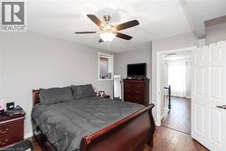 Bedroom featuring wood-finish flooring, a ceiling fan with integrated lighting, and a window with brick exterior visibility - 