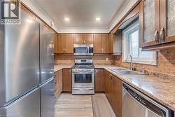 Kitchen featuring wood cabinetry, stainless steel appliances, a tiled backsplash, and stone-finish countertops - 