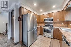 Kitchen featuring stainless steel appliances, wood-finish cabinetry, a tile backsplash, and composite countertops - 