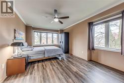 Spacious room featuring wood-finish flooring, two large window sets, crown molding, and a ceiling fan with integrated lighting - 