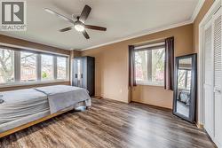 Spacious room featuring wood-finish flooring, a contemporary ceiling fan, and multiple windows with roller blinds - 