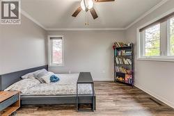 Spacious room featuring wood-finish flooring, two large windows for natural light, a ceiling fan with integrated lighting, and crisp white crown molding - 