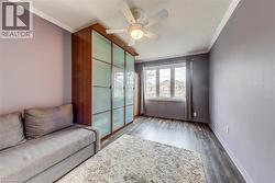 Room featuring wood-finish flooring, a built-in wardrobe with frosted glass panels, a ceiling fan with integrated lighting, and crown molding - 
