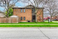 Brick exterior home featuring a wood privacy fence, a detached shed, established trees, and a manicured lawn - 