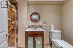 Compact bathroom featuring a shower with brown tile surround, a dark wood vanity with frosted glass doors, a white integrated sink, and a decorative tile backsplash - 