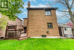 Expansive rear exterior featuring a brick facade, a multi-level wood-finish deck with privacy lattice, a detached storage shed, a green lawn, and mature trees - 
