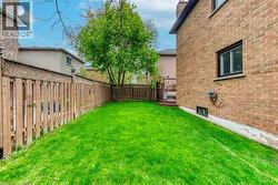 Expansive rear yard featuring green lawn, a privacy fence, mature trees, and a wooden deck - 